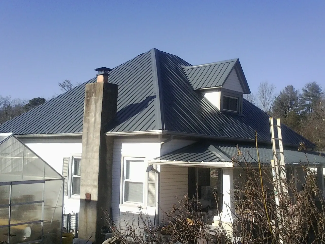 Dark blue standing seam metal roof on a white farmhouse with dormer — Slate & Tile Roof Repair by Roofing Brothers in Logsden