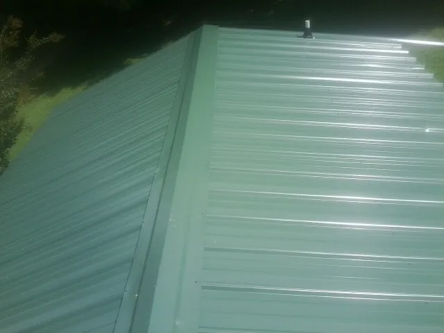 New green metal panels meeting at the ridge of a roof — Flat Roof Repair work by our crew in Logsden