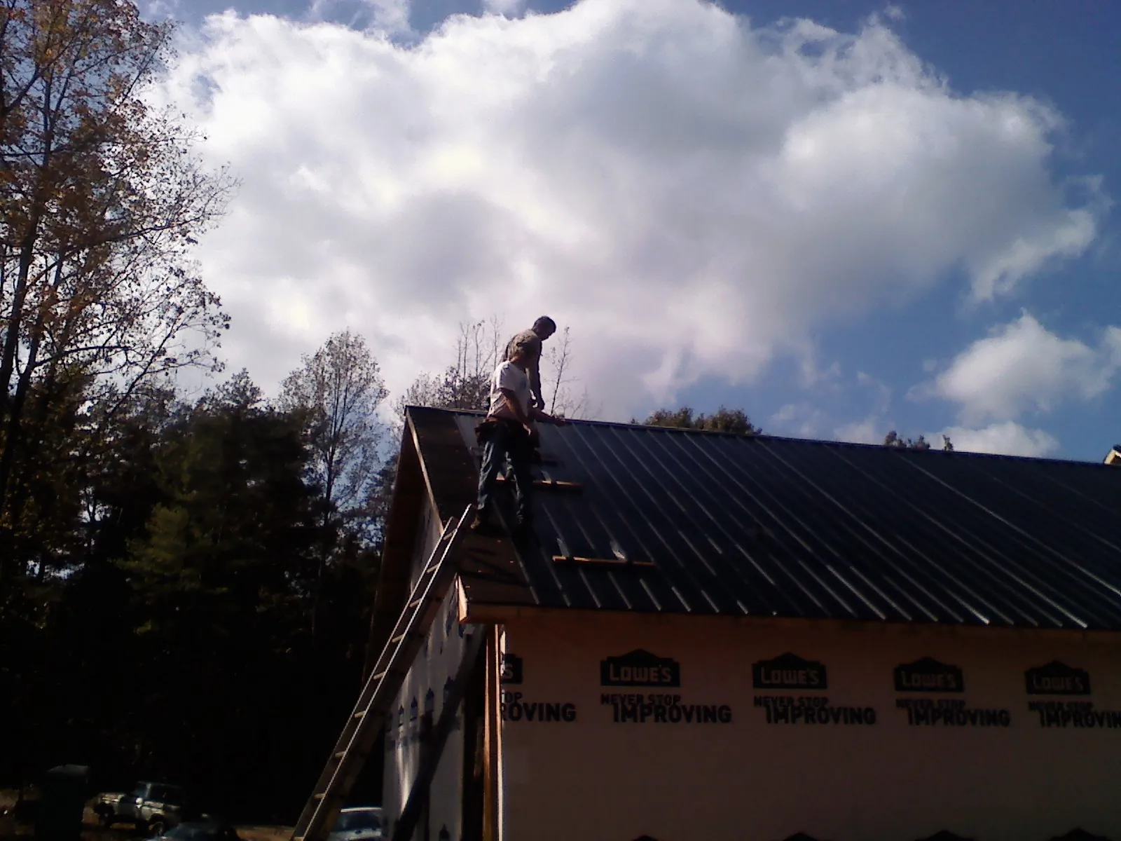 Roofer fastening dark metal panels high against a cloudy sky, from a Roof Inspection job in Logsden