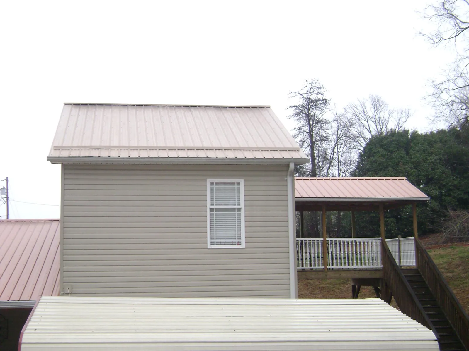 Tan metal roofs on a two story addition and attached porch, from a Roof Replacement job in Logsden